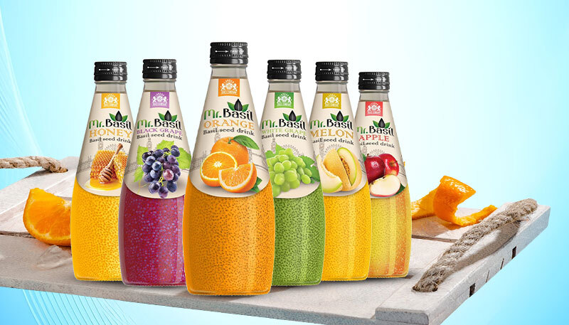 Assorted Mr. Basil basil seed beverage bottles with fruit flavors arranged on a tray with fresh orange slices.